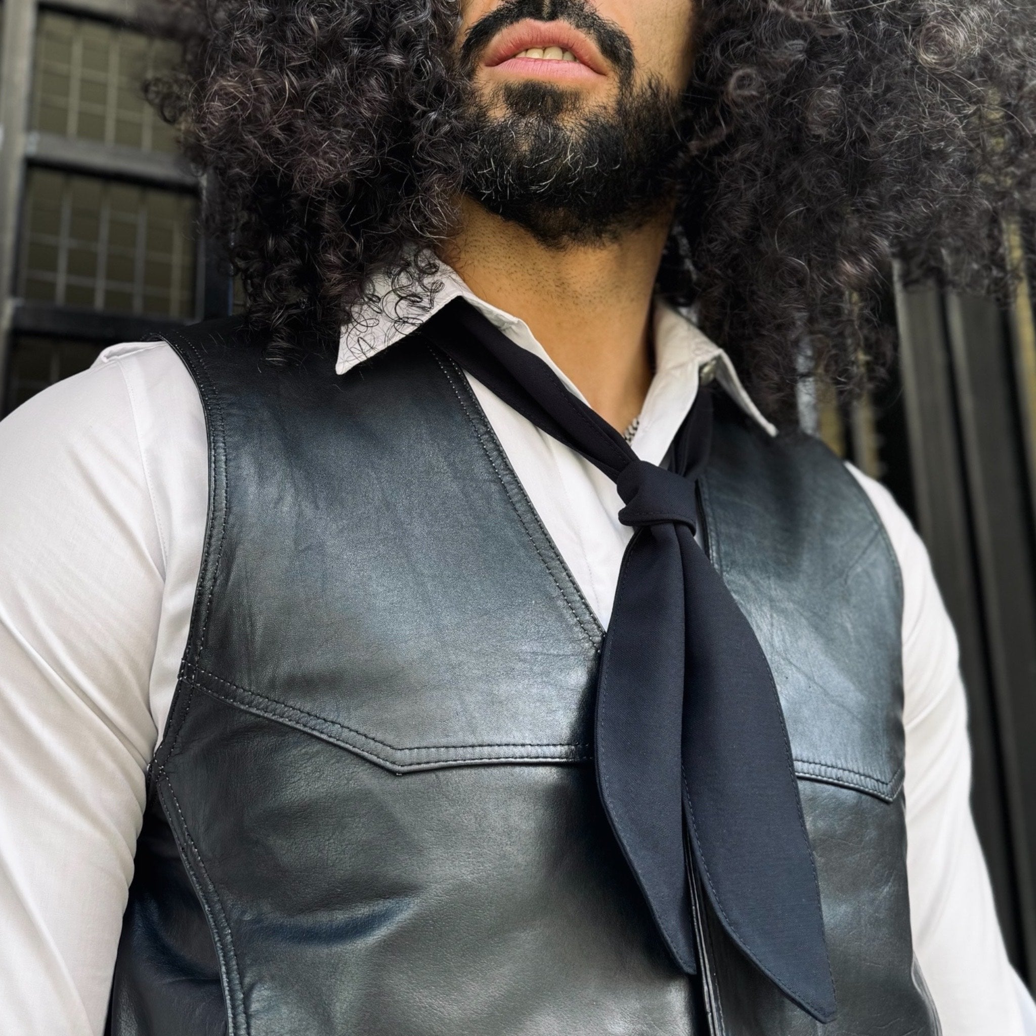 Man wearing a leather vest and dark tie with a blurred background