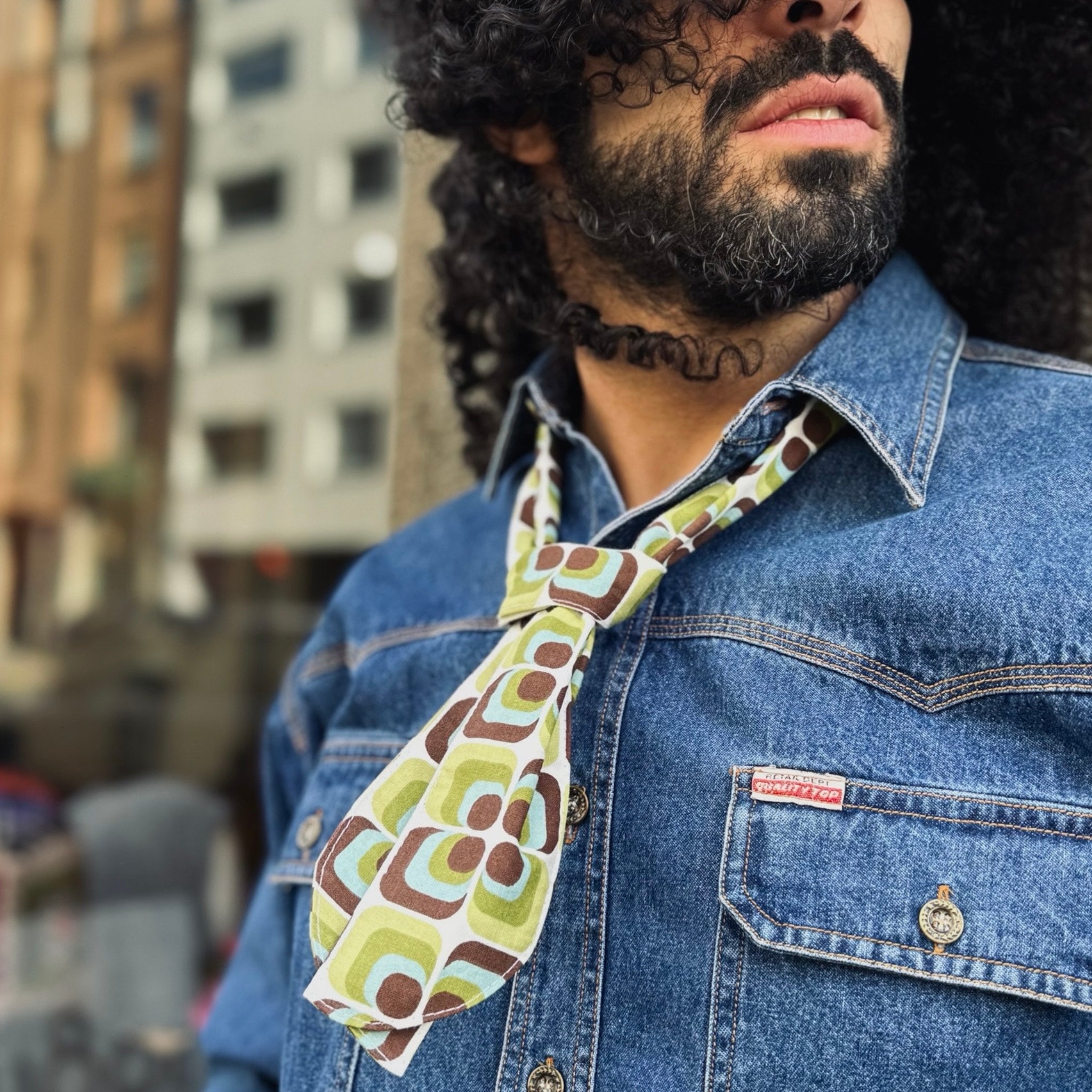 Man wearing a patterned neckerchief and denim jacket in an urban setting